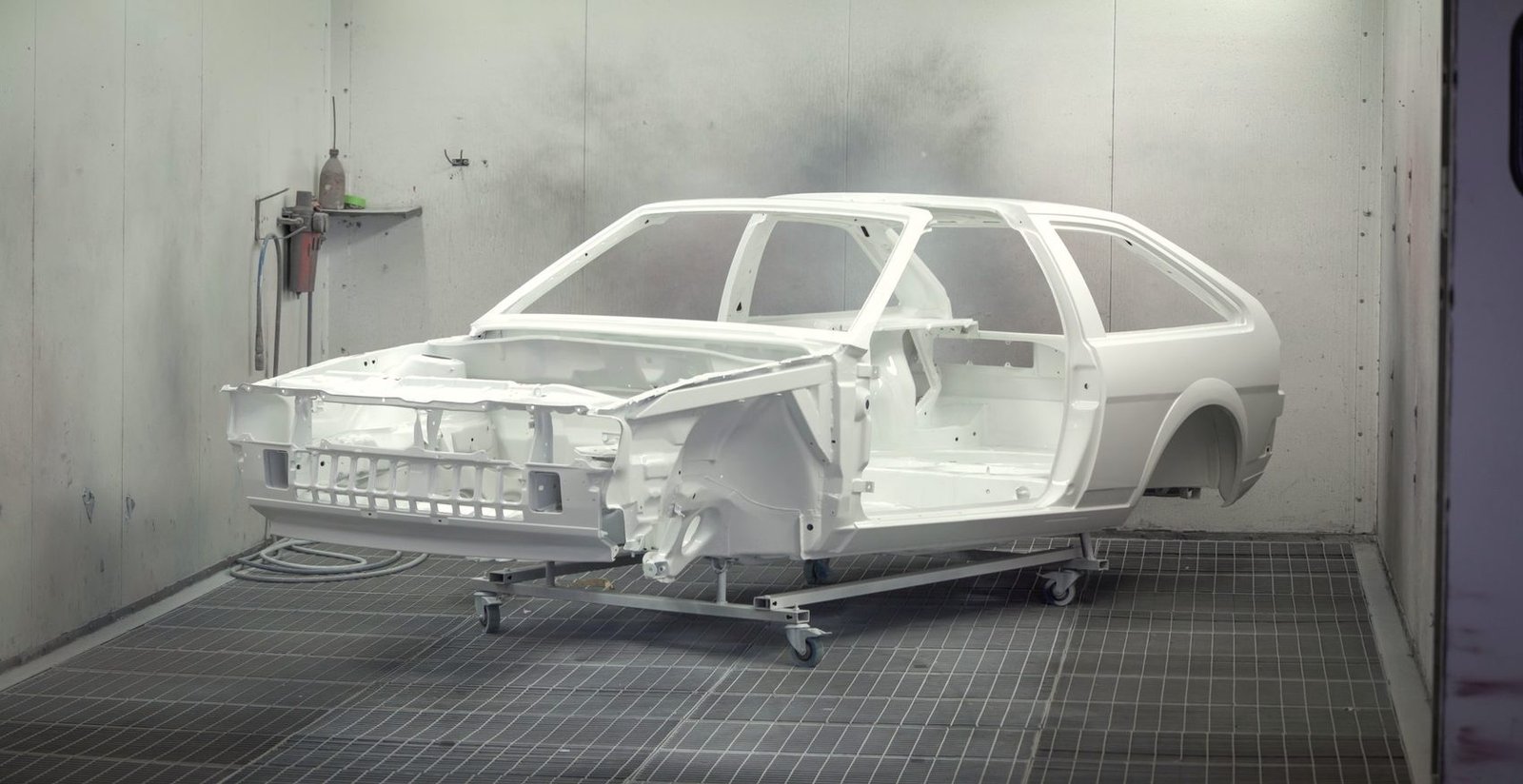 A bare car shell in white primer on a dolly inside a paint booth