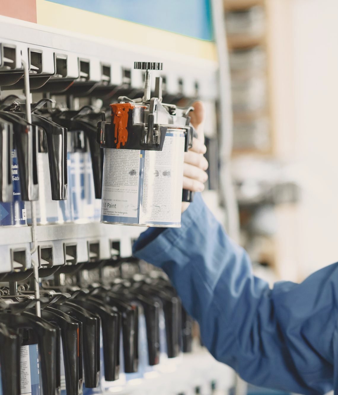 A hand in a blue work sleeve lifting a paint mixing cup from a rack of toners