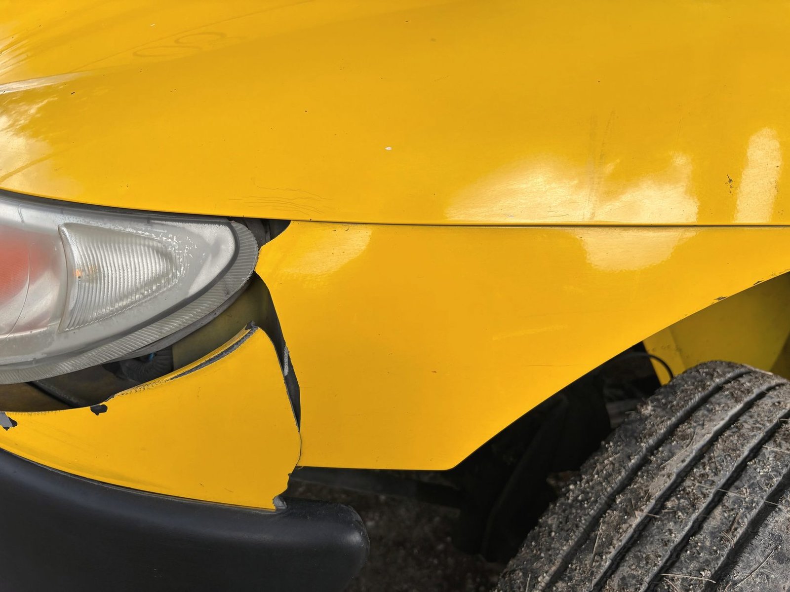 Close view of a yellow car with a crushed front corner and a displaced headlight