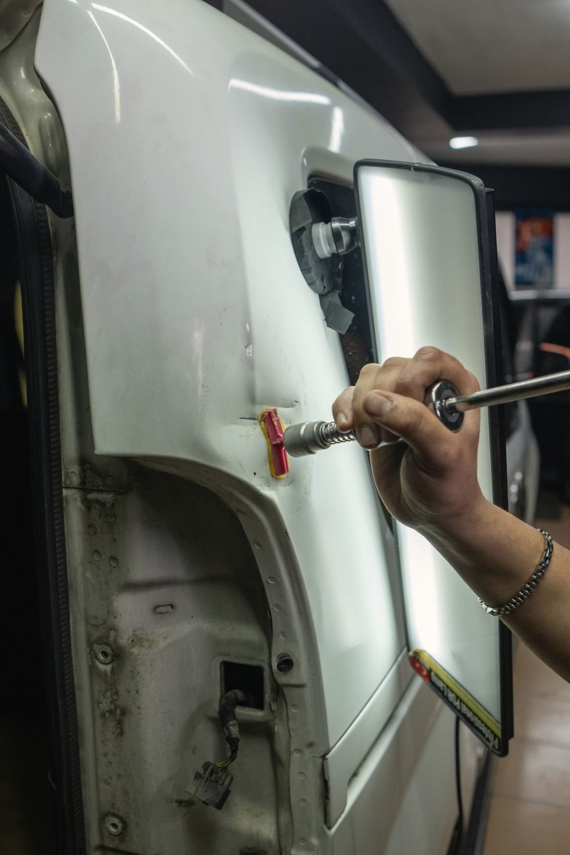 A hand working a dent out of a white rear quarter panel beside a reflection board