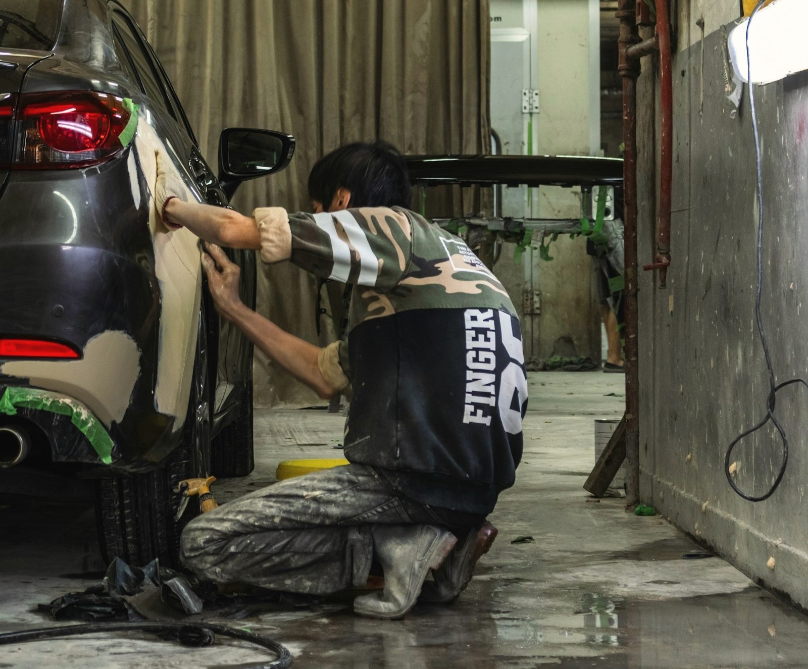 A person kneeling to block sand filler on the rear quarter of a grey car