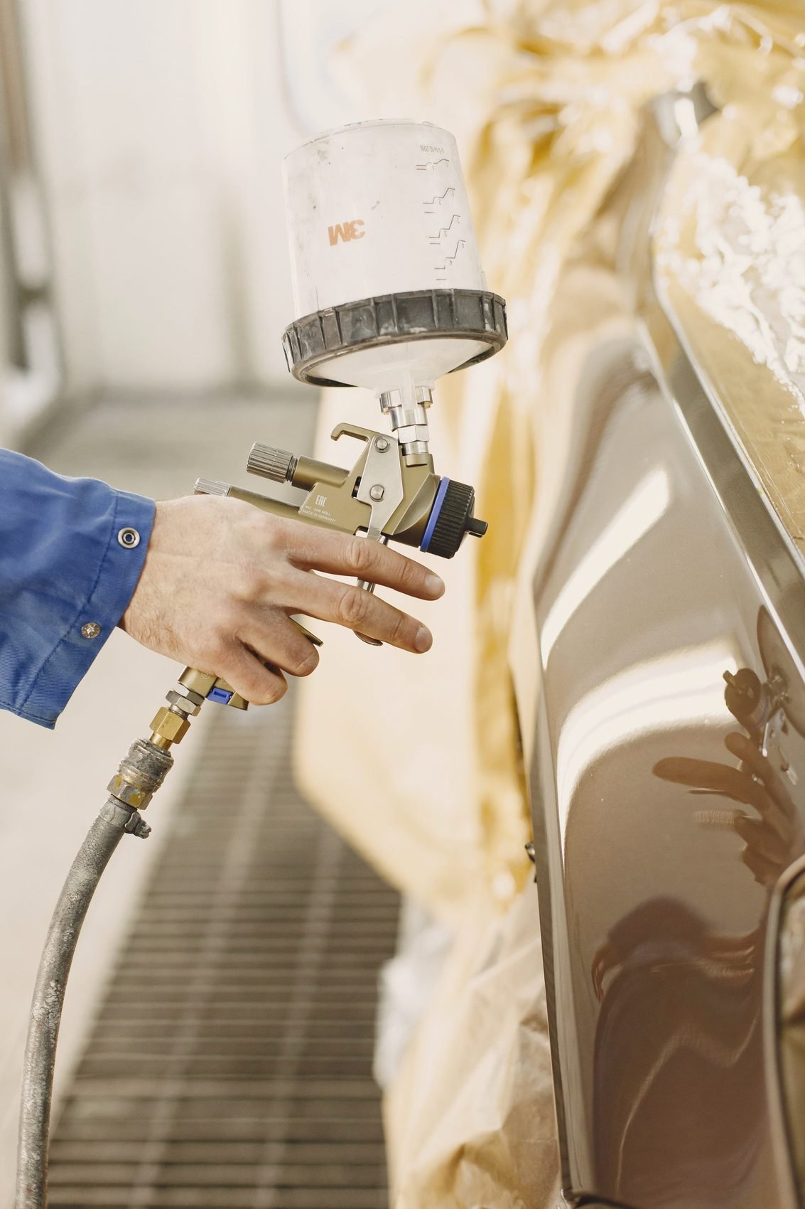 A gloved hand holding a spray gun against a masked car in a paint booth